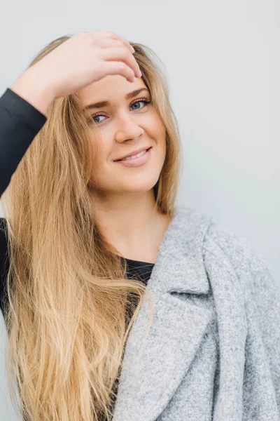 Loira jovem mulher de pé atrás da parede e posando câmera ti — Fotografia de Stock