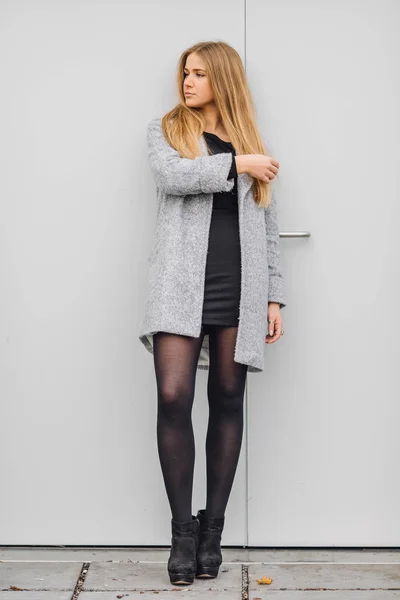 Blonde young woman standing behind the wall and posing ti camera