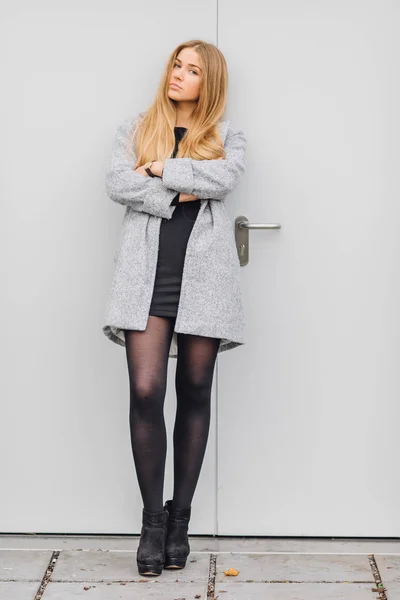 Blonde young woman standing behind the wall and posing ti camera