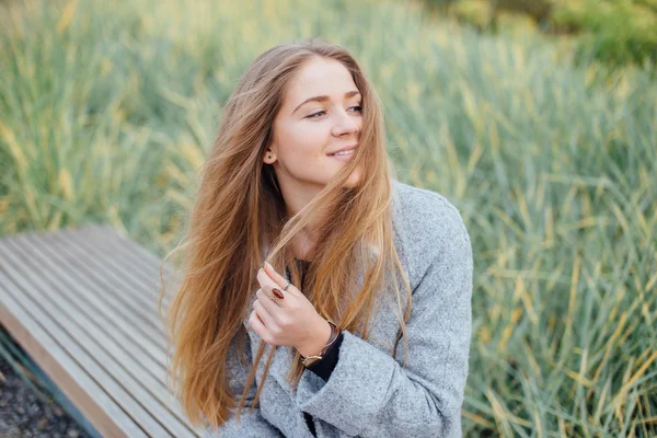 Blonda hår kvinna sitter på bänken och leende — Stockfoto