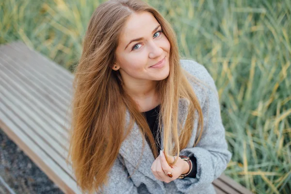 Mulher de cabelo loiro sentado no banco e sorrir — Fotografia de Stock