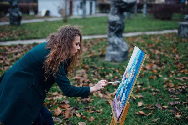 Young woman drawing in easel on the park background — Stock Photo, Image