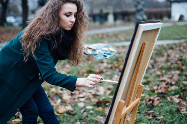 Молодая женщина рисует мольбертом на фоне парка — стоковое фото