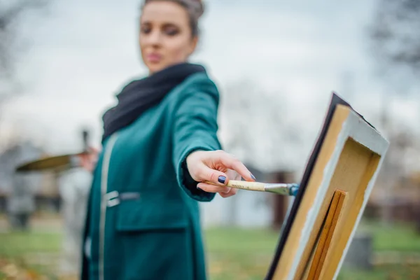 Молодая женщина рисует мольбертом на фоне парка — стоковое фото