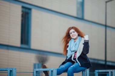 Young girl sitting on the metal bench near modern architecture