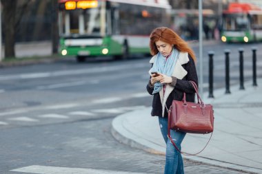 Red-haired girl walking on the street and listen music on her phone