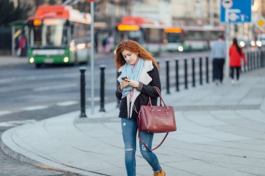 Red-haired girl walking on the street and listen music on her phone