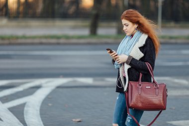 Red-haired girl walking on the street and listen music on her phone