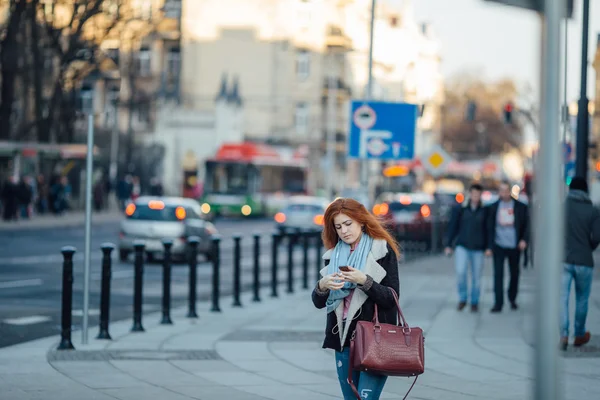 Ragazza dai capelli rossi che cammina per strada e ascolta musica sul suo telefono — Foto Stock