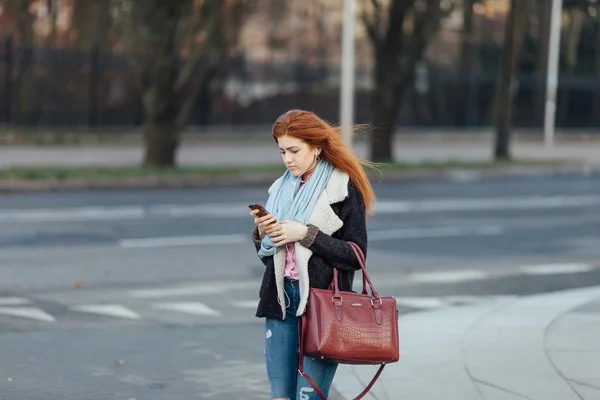 Fille aux cheveux roux marchant dans la rue et écouter de la musique sur son téléphone — Photo