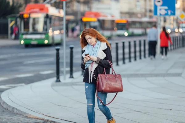 Red-haired girl walking on the street and listen music on her phone — 图库照片
