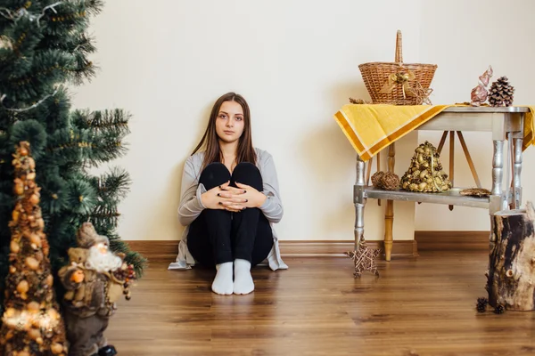 Menina solitária sentada atrás da árvore de Natal com presentes — Fotografia de Stock