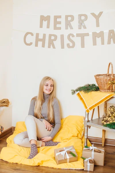 Blonde jeune fille assise près du mur et ouvrant ses cadeaux — Photo