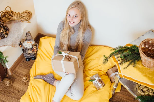 Blond, ung jente som sitter ved veggen og åpner gavene sine – stockfoto