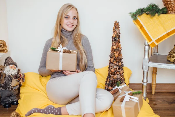 Blond, ung jente som sitter ved veggen og åpner gavene sine – stockfoto