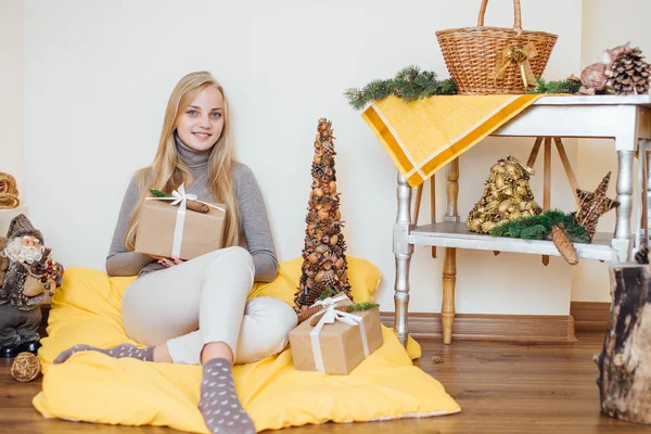 Blond, ung jente som sitter ved veggen og åpner gavene sine – stockfoto