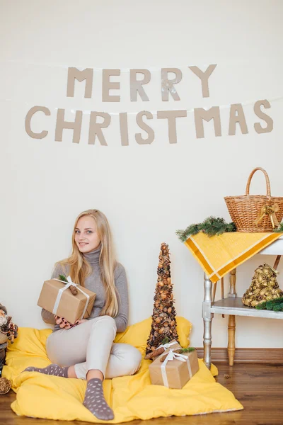 Blond, ung jente som sitter ved veggen og åpner gavene sine – stockfoto