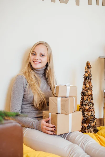 Blond, ung jente som sitter ved veggen og åpner gavene sine – stockfoto