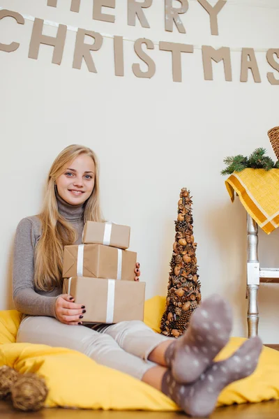 Blonde jeune fille assise près du mur et ouvrant ses cadeaux — Photo