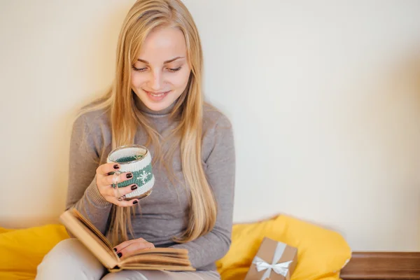 Blond meisje drinkig haar koffie, eten cookies en een boek lezen — Stockfoto
