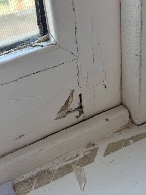 Hasarlı bir pencere çerçevesinin yakından görüntüsü boyaların soyulduğunu ve yüzeydeki çatlakların yaşını ve yıprandığını gösteriyor..