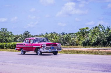 Havana, Küba - 17 Temmuz 2018: Berrak mavi bir gökyüzü altında Havana Küba 'da yemyeşil otobanı boyunca uzanan canlı kırmızı klasik bir araba sürüyor.
