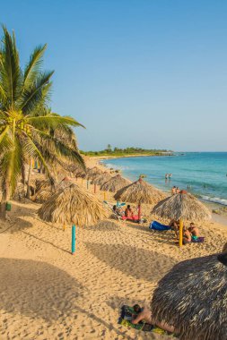 Trinidad, Küba - 17 Temmuz 2018: Ziyaretçiler, Küba 'nın Trinidad plajında kumlu sahildeki saman şemsiyelerin altında güneşli bir günün tadını çıkarıyorlar.