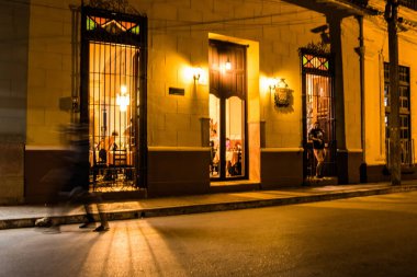 Trinidad, Küba - 16 Temmuz 2018: İnsanlar akşamlarını Trinidad kafesinde geçirirken, yoldan geçen biri alacakaranlıkta Küba sokaklarında yürüyor..