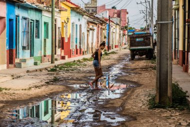 Trinidad, Küba - 15 Temmuz 2018: Trinidad Küba 'da canlı renkli evlerle çevrili çamurlu bir yolda çıplak ayakla su birikintilerinde yürüyen genç bir kadın.