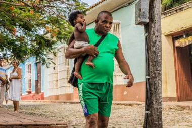 Trinidad, Küba - 15 Temmuz 2018: Trinidad Küba 'da kaldırım taşı caddesinde bir adam omzunda bir çocuk taşıyor. Etraflarını saran canlı binalar..