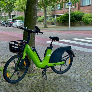 Hollanda, den haag - 23 Mayıs 2024: Elektrikli bisiklet ya da bisiklet paylaşım sistemi adı verilen caddeye park edilmiş bir ağacın yanına git