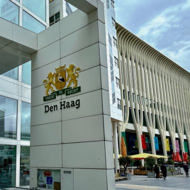 Hollanda - 25 Nisan 2024: İnsanlar adalet ve barış şehrinin modern beyaz mimari belediye binasına açık logo ve belediye mührü ile giriyorlar.