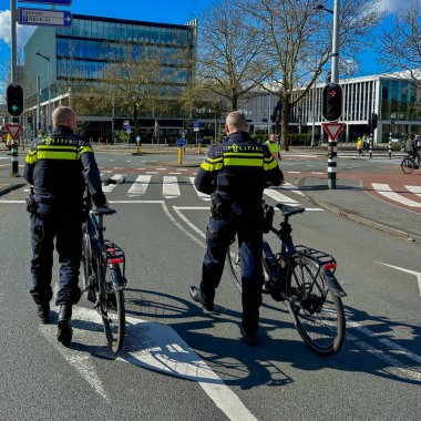 Amsterdam, Hollanda - 7 Nisan 2024: Hollanda Ulusal Polisi bisikletlerinin yanında bisiklet kaskıyla yürüyor
