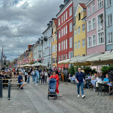 Kopenhag, Danimarka - 24 Temmuz 2023: Ziyaretçiler renkli evleri ve klasik tekneleriyle nyhavn ünlü limanında yürüyorlar