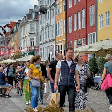 Kopenhag, Danimarka - 24 Temmuz 2023: Ziyaretçiler renkli evleri ve klasik tekneleriyle nyhavn ünlü limanında yürüyorlar