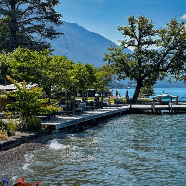 Talloire, Fransa - 25 Haziran 2023: Ek Dağ Gölü kıyısındaki bir restoranın teras masaları ve şemsiyeleri