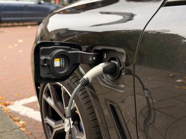 Den Haag, Hollanda - 19 Ekim 2025: Şehrin bir bölgesinde modern teknoloji ve sürdürülebilir ulaşım seçeneklerini gösteren bir konnektörle elektrikli araç şarj ediliyor.