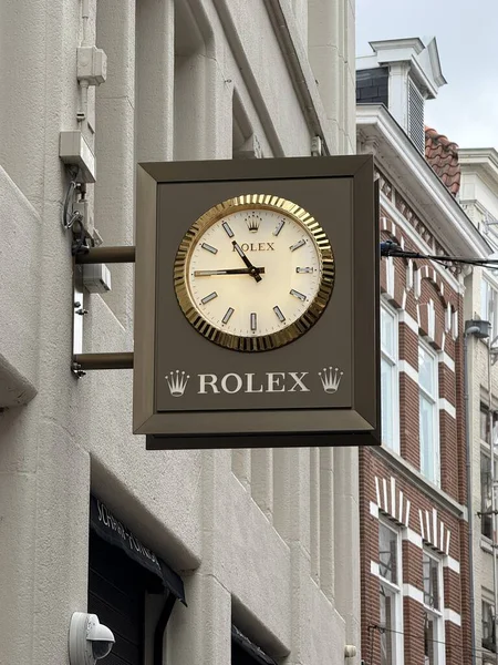 Hollanda, Hollanda 28 Temmuz 2025: Bulutlu bir günde klasik mimarisi olan bir şehirdeki bir mağazanın duvarına monte edilen saati gösteren bir Rolex saat.