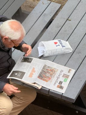 Lahey, Hollanda - 27 Eylül 2025: Lahey 'de bir bankta oturan yaşlı bir adam, hareketli kentte huzurlu bir anın keyfini çıkarıyor.