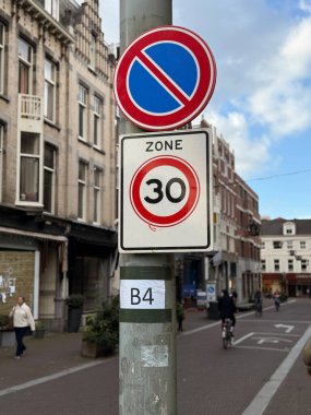 Den Haag, Hollanda - 22 Eylül 2025: Trafik işaretleri, bina ve yayaların bulunduğu bir şehir caddesinde park yasağı ve hız sınırının 30 km olduğunu gösteriyor.