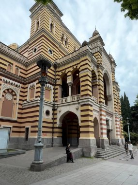 Tiflis, Gürcistan - 25 Nisan 2025: Ziyaretçiler, Tiflis 'teki zengin kültür mirasını sergileyen tarihi bir binanın eşsiz çizgili mimarisine hayran kaldılar.