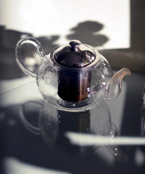 Чайник с чаем, стоящим на столе прозразном. Стеклянный стол. Чаепитие  . — стоковое фото