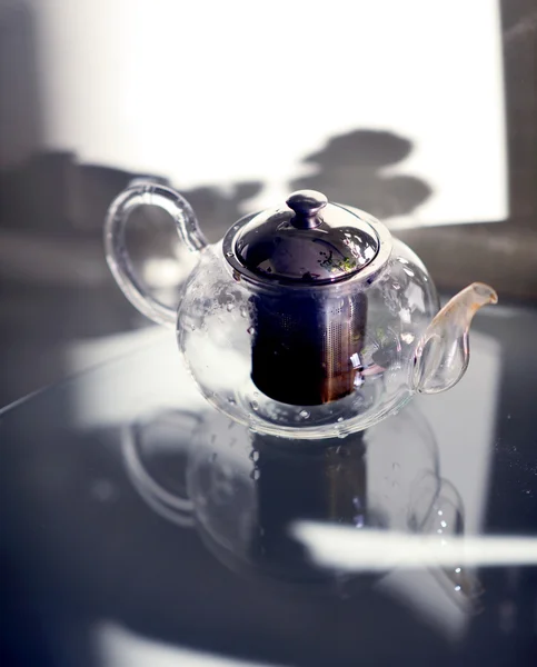 Чайник с чаем, стоящим на столе прозразном. Стеклянный стол. Чаепитие  . — стоковое фото