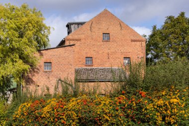 Kırmızı tuğladan yapılmış tipik bir bina manzarası. Kuzey Almanya 'nın her yerinde bulunur. Binanın önünde sonbahar mevsiminde sarı ve kırmızı böğürtlenli bir çalı ağacı görebilirsiniz..