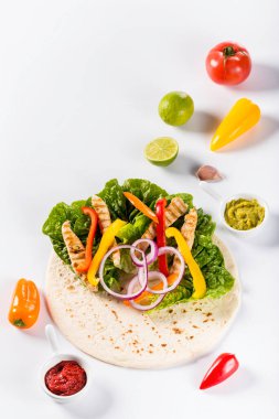 Tortilla 'yı taze sebze, tavuk ve sosla hazırlamak için gerekli malzemeler. Beyaz arkaplanda düz görünüm.
