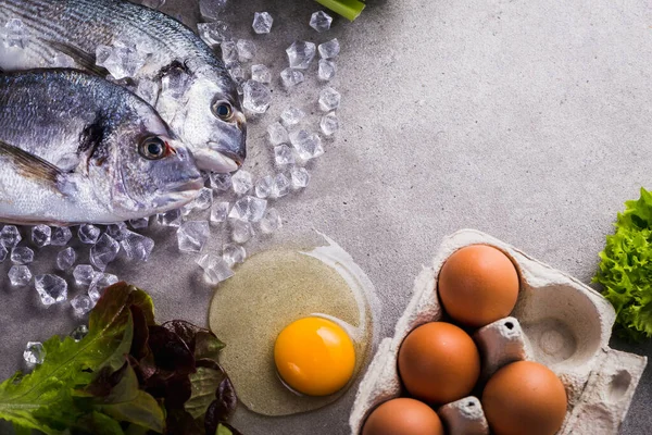 おいしいと健康的な食品のための生の調理成分のフレーム 氷の上の新鮮なDorado魚 灰色のコンクリートの背景に卵 Top View — ストック写真