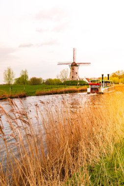 Gün batımında değirmeni olan nehirde eski bir tekne. Belçika 'nın Damme kasabası