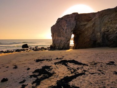 Sahilde, koca bir kayanın üzerinde gün batımı.