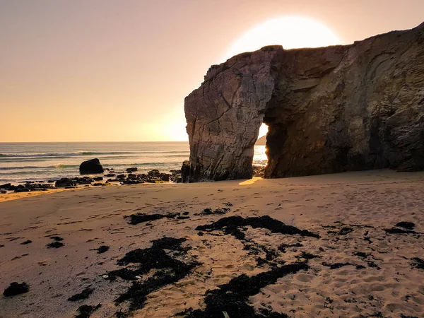 Sahilde, koca bir kayanın üzerinde gün batımı.