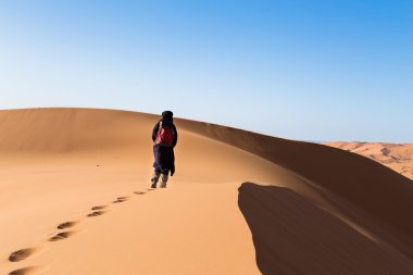 One male tuareg climbing a dune in the desert. clipart